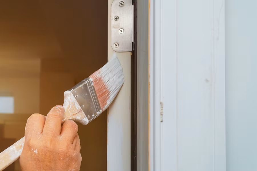 Worker painting white door frame with brush and paint