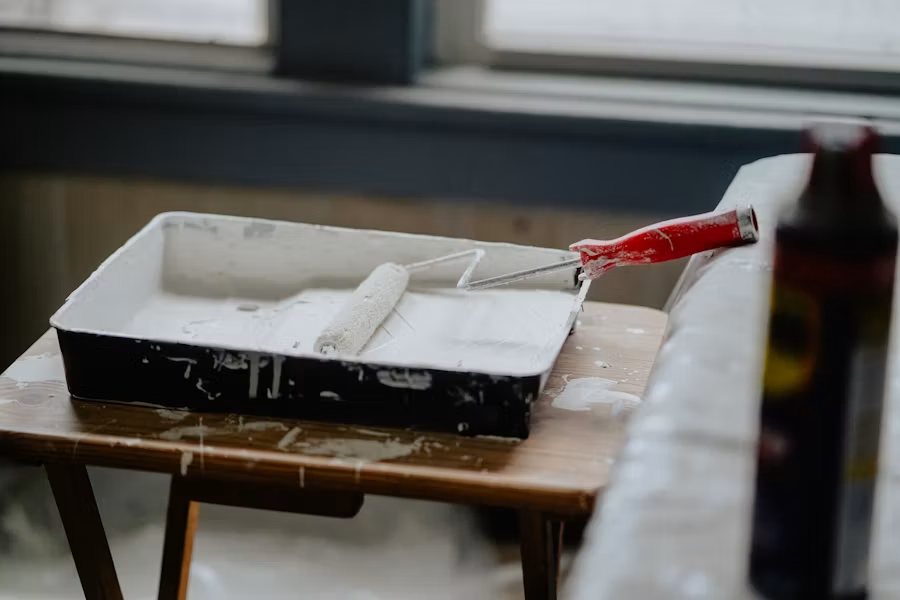 Paint tray and roller with red-handled brush on wooden surface during interior painting project