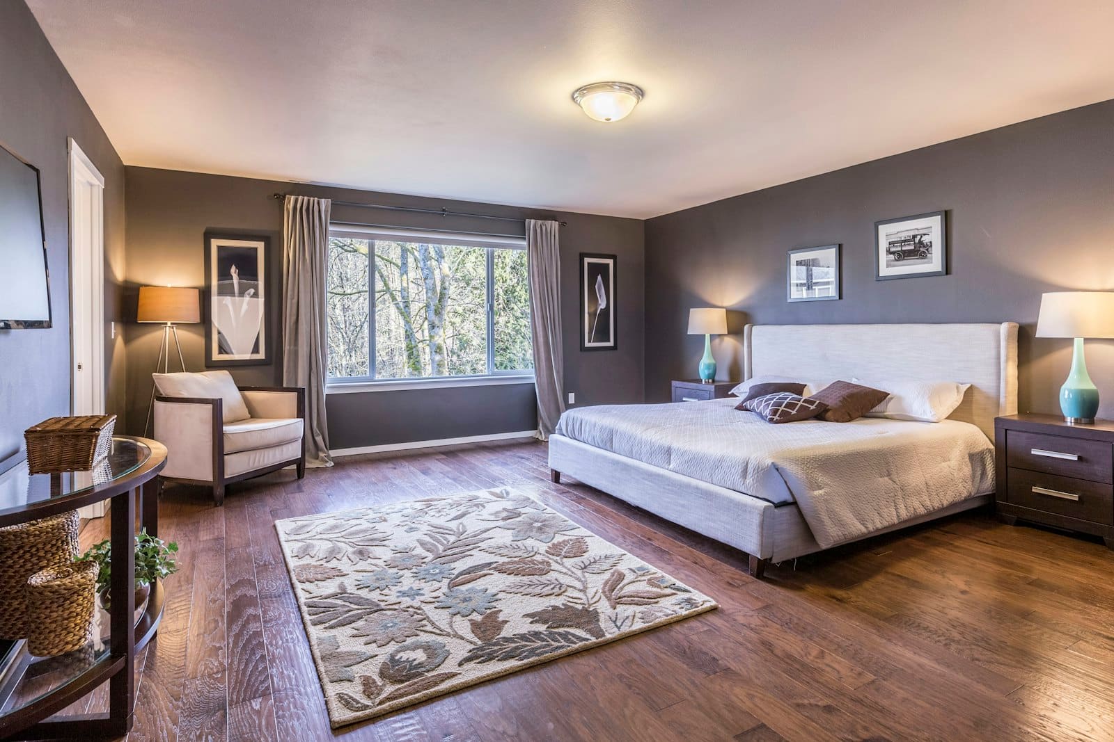 Spacious master bedroom with white bed, purple walls, hardwood floors, large windows, and sitting area