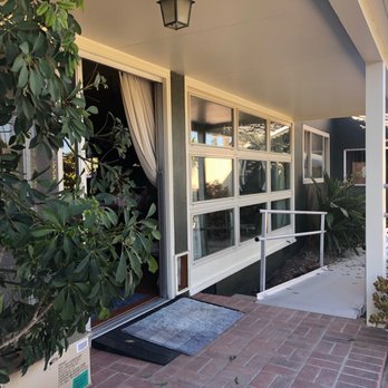 Storefront entrance with glass doors, potted plants, and brick patio leading to shop interior