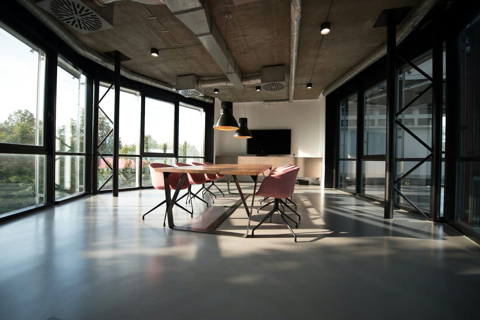 Modern office meeting room with wooden table, burgundy chairs, and floor-to-ceiling windows overlooking trees