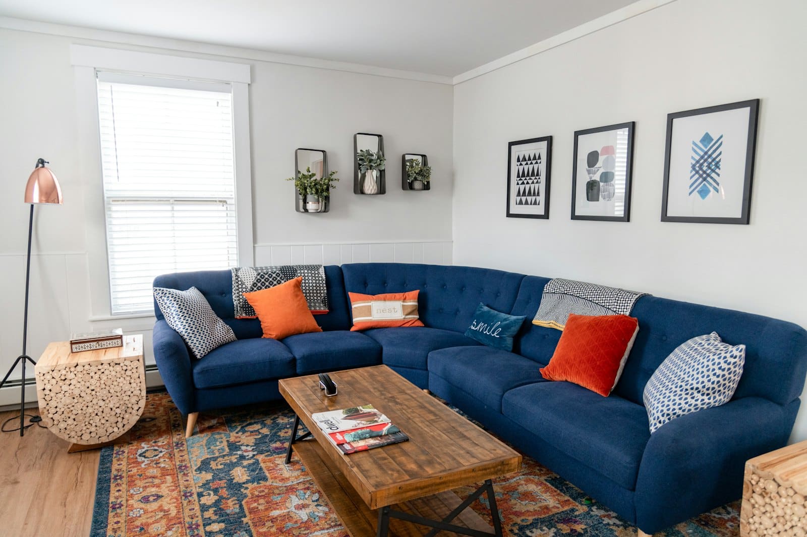 Modern living room with navy blue sectional sofa, orange pillows, wooden coffee table, and framed wall art